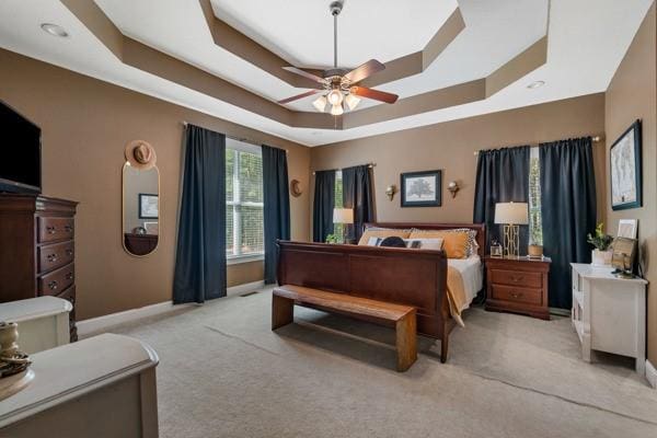 bedroom with ceiling fan, light colored carpet, and a tray ceiling