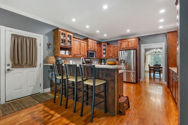 kitchen with a breakfast bar, light hardwood / wood-style flooring, ornamental molding, appliances with stainless steel finishes, and kitchen peninsula