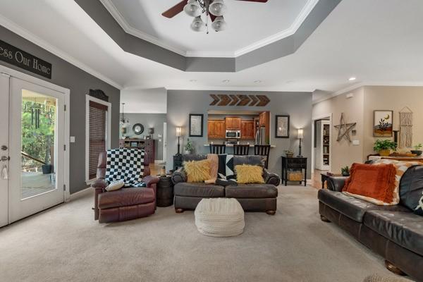 carpeted living room with french doors, a raised ceiling, ceiling fan, and crown molding