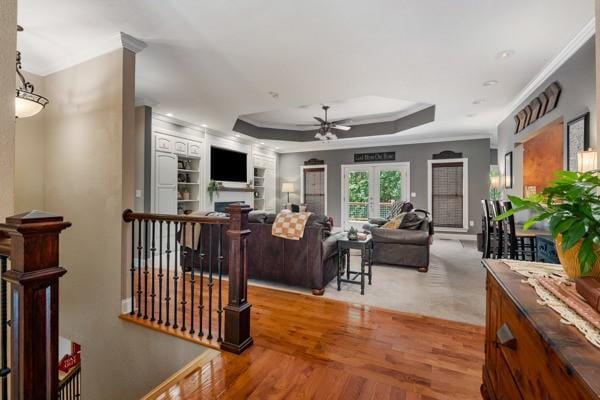 living room with a raised ceiling, ceiling fan, wood-type flooring, and ornamental molding