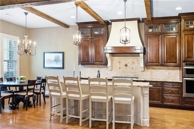 kitchen featuring light stone counters, a breakfast bar area, decorative light fixtures, and custom exhaust hood