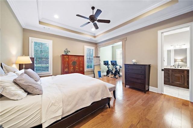 bedroom with ensuite bath, light wood-type flooring, ornamental molding, a raised ceiling, and ceiling fan