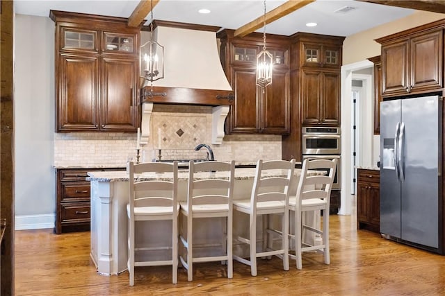 kitchen with a center island with sink, light wood-type flooring, appliances with stainless steel finishes, light stone countertops, and decorative backsplash