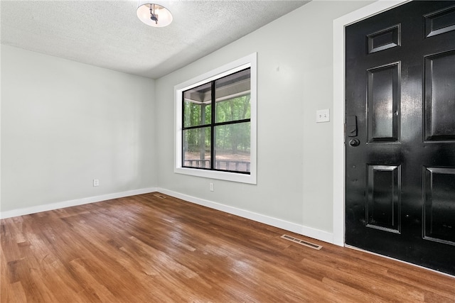 unfurnished room featuring baseboards, visible vents, wood finished floors, and a textured ceiling