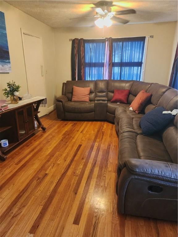 living room with hardwood / wood-style flooring, ceiling fan, and a textured ceiling