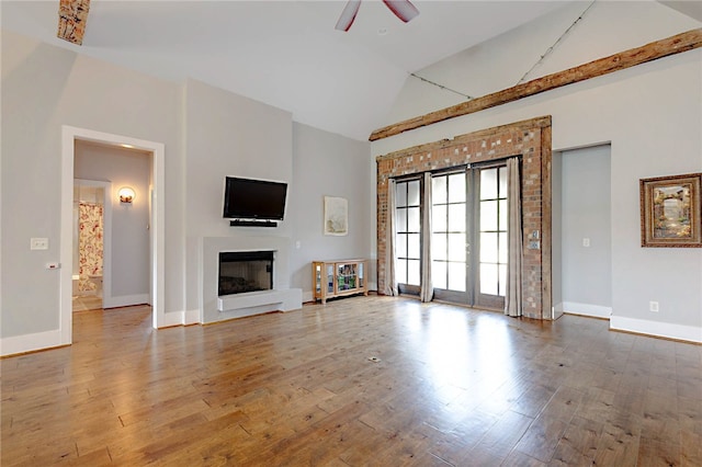 unfurnished living room featuring baseboards, a glass covered fireplace, ceiling fan, high vaulted ceiling, and hardwood / wood-style flooring