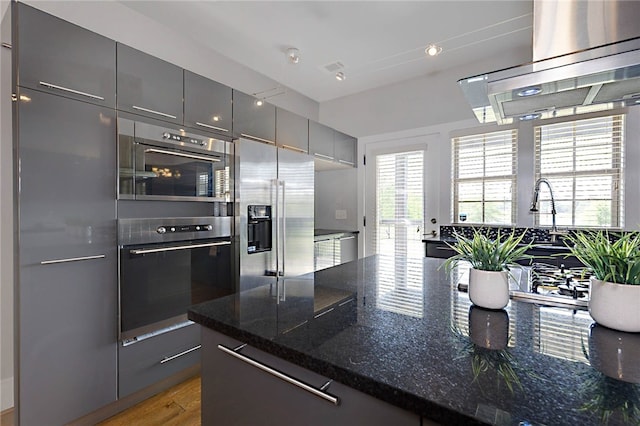 kitchen featuring dark stone counters, extractor fan, gray cabinets, modern cabinets, and high end refrigerator