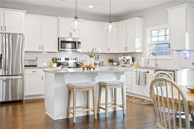 kitchen featuring a center island, hanging light fixtures, stainless steel appliances, light stone countertops, and white cabinets