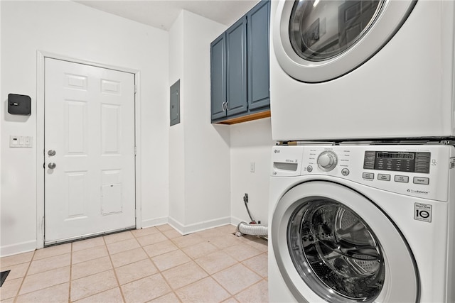 laundry area featuring stacked washer and dryer, light tile patterned floors, and cabinets