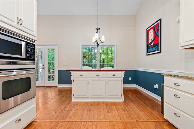 kitchen featuring pendant lighting, an inviting chandelier, white cabinets, light hardwood / wood-style floors, and stainless steel microwave