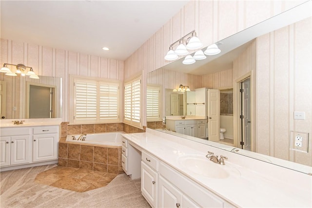 bathroom with toilet, vanity, and tiled bath