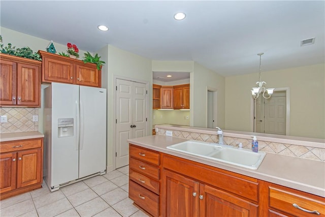 kitchen with decorative light fixtures, a notable chandelier, white fridge with ice dispenser, backsplash, and sink