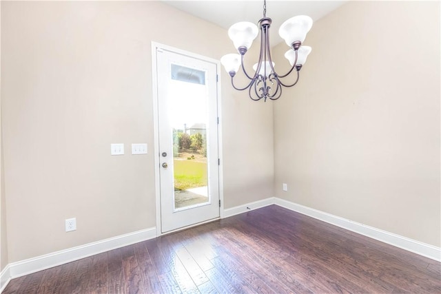 unfurnished dining area featuring a chandelier, dark wood-style flooring, and baseboards