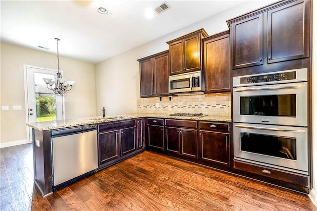 kitchen featuring appliances with stainless steel finishes, a sink, a peninsula, a chandelier, and dark wood-style floors