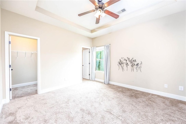 unfurnished bedroom featuring a raised ceiling, carpet floors, baseboards, and a spacious closet