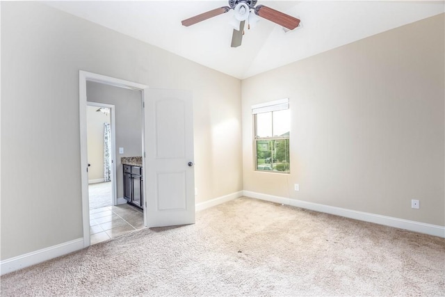 spare room featuring light colored carpet, a ceiling fan, vaulted ceiling, and baseboards