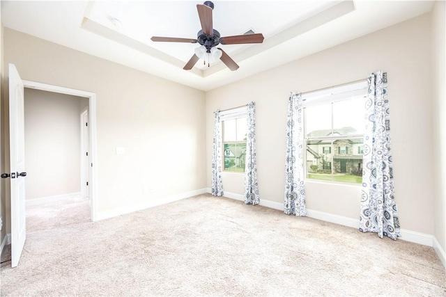 carpeted spare room with a raised ceiling, baseboards, and a ceiling fan