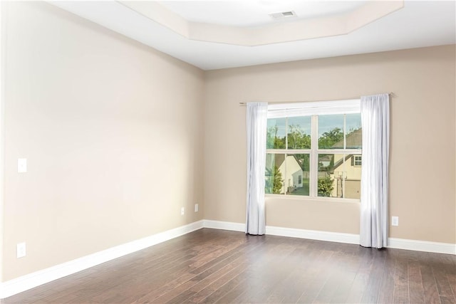 spare room featuring dark wood finished floors, a raised ceiling, and baseboards