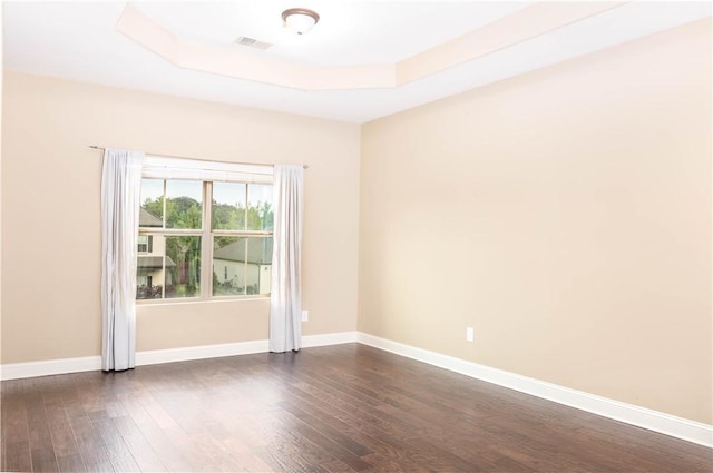 spare room with dark wood-style flooring, a raised ceiling, and baseboards