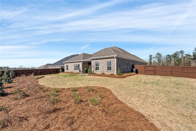 back of house featuring brick siding, roof with shingles, a fenced backyard, and a lawn