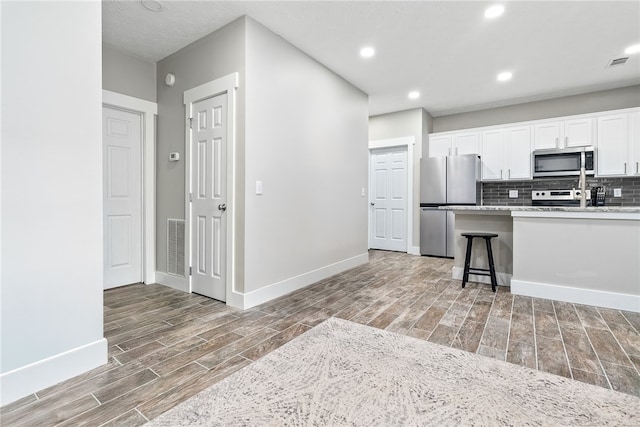 303 N Ross St Unit 104, Auburn, AL 36830 - kitchen featuring stainless steel appliances, light wood-type flooring, baseboards, white cabinetry, and decorative backsplash