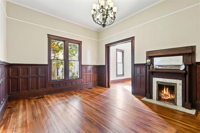 interior space with crown molding, a stone fireplace, hardwood / wood-style floors, and a notable chandelier