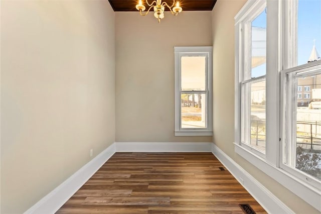 spare room with an inviting chandelier and dark wood-type flooring