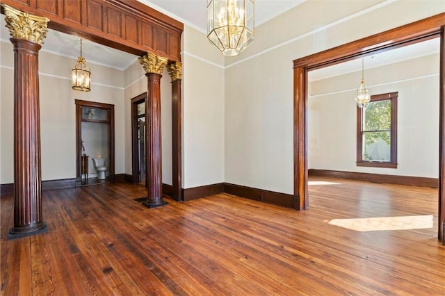 spare room featuring an inviting chandelier, ornamental molding, dark hardwood / wood-style floors, and ornate columns