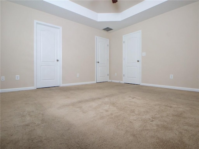 spare room with a tray ceiling, carpet flooring, visible vents, and baseboards