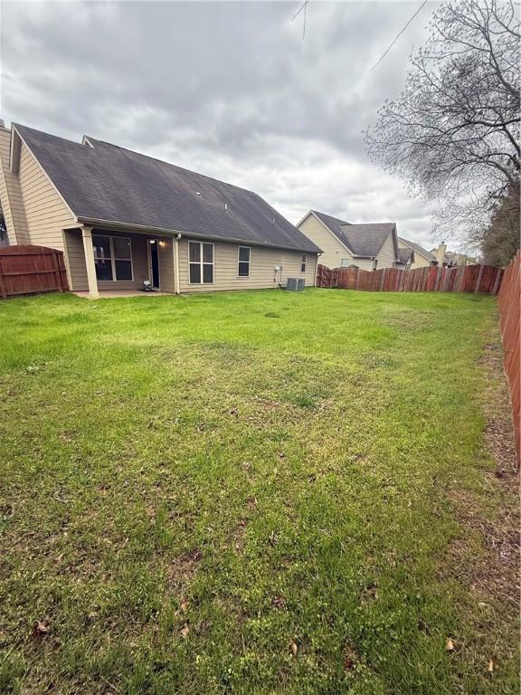 rear view of property featuring a fenced backyard, cooling unit, and a lawn