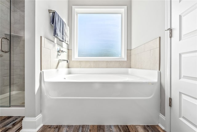 full bathroom featuring a shower stall, a bath, and wood finished floors