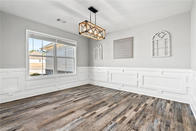 unfurnished dining area featuring wainscoting, dark wood finished floors, visible vents, and an inviting chandelier