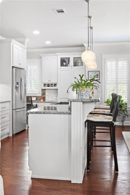 3412 Double Eagle Ln, Opelika, AL 36801 - kitchen with stainless steel fridge, ornamental molding, light stone counters, white cabinetry, and a kitchen bar