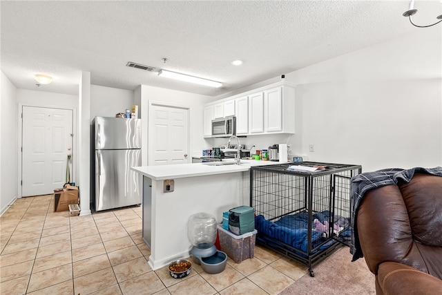 kitchen with appliances with stainless steel finishes, white cabinetry, light tile patterned floors, kitchen peninsula, and a textured ceiling