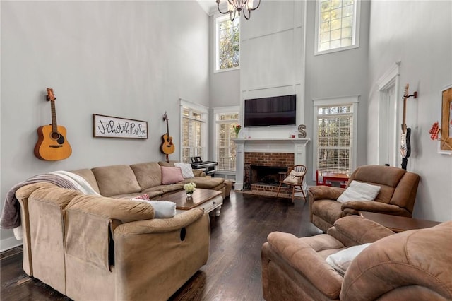 living room with dark wood-type flooring, a high ceiling, an inviting chandelier, and a fireplace