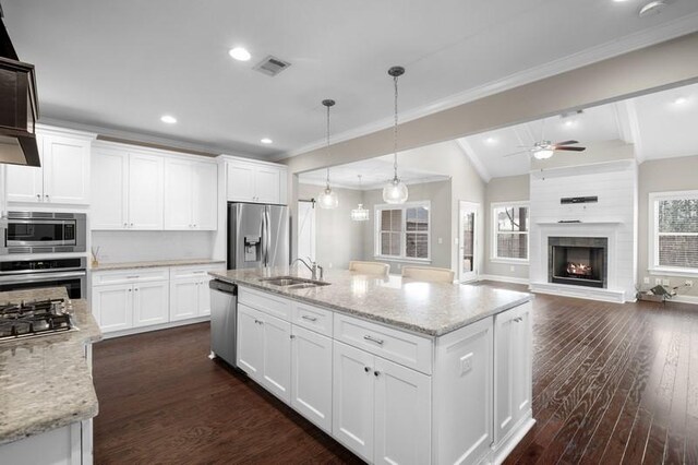 kitchen featuring white cabinetry, light stone counters, hanging light fixtures, a center island with sink, and stainless steel appliances