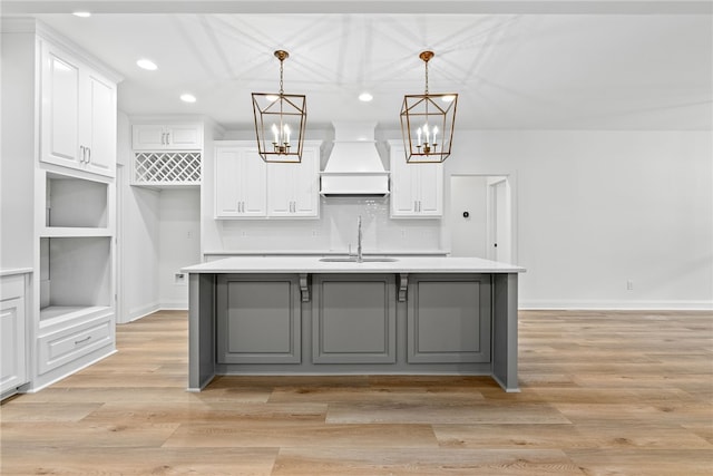 kitchen with pendant lighting, white cabinetry, custom range hood, and a kitchen island with sink