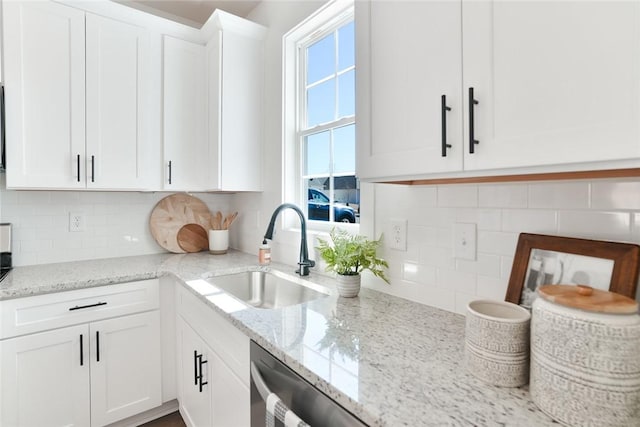 kitchen with a sink, light stone counters, tasteful backsplash, and white cabinetry