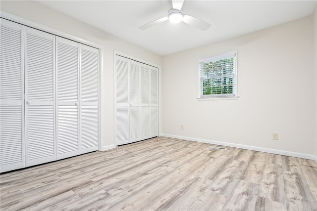 unfurnished bedroom with two closets, ceiling fan, baseboards, and light wood-style floors