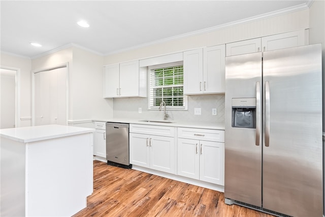 kitchen with light wood finished floors, ornamental molding, a sink, appliances with stainless steel finishes, and white cabinetry