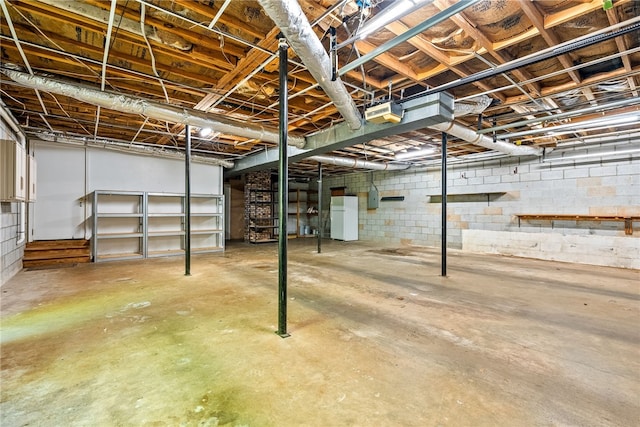 unfinished basement featuring concrete block wall and freestanding refrigerator