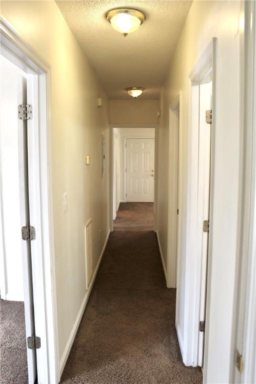 hallway featuring visible vents, dark carpet, a textured ceiling, and baseboards