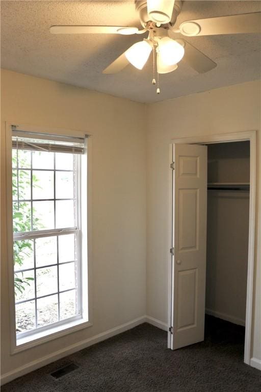 unfurnished bedroom with dark colored carpet, multiple windows, visible vents, and baseboards