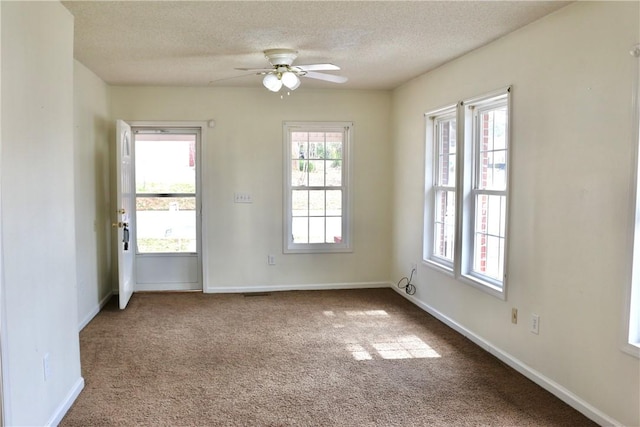 spare room featuring a textured ceiling, dark colored carpet, baseboards, and a healthy amount of sunlight