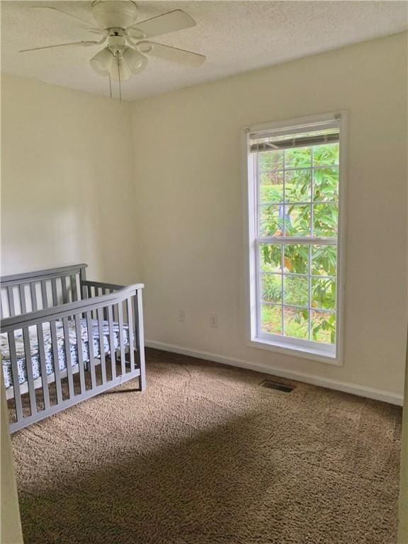 carpeted bedroom featuring ceiling fan and a nursery area