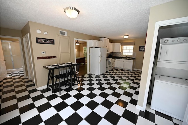 kitchen featuring a textured ceiling, white appliances, sink, white cabinets, and stacked washer and dryer