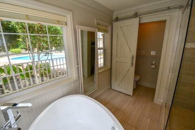 bathroom featuring plenty of natural light, ornamental molding, and a tub to relax in