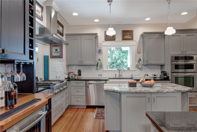 kitchen featuring appliances with stainless steel finishes, sink, hanging light fixtures, and wall chimney range hood