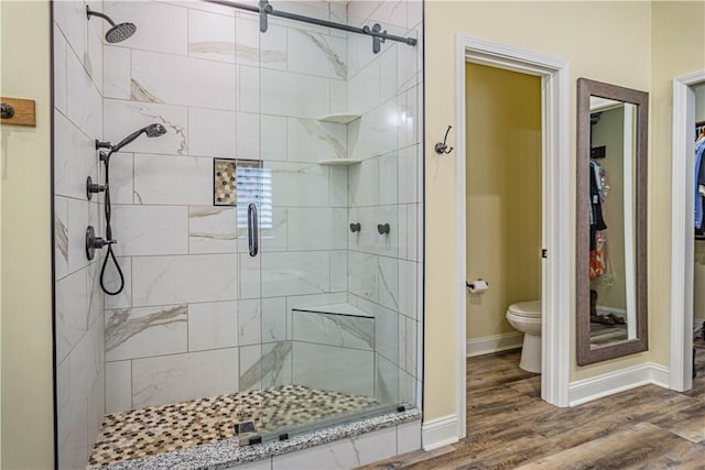 bathroom featuring baseboards, wood finished floors, toilet, and a stall shower