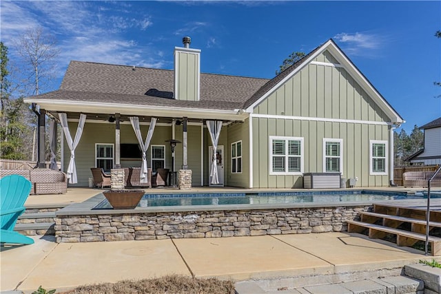 back of house with a patio, a ceiling fan, roof with shingles, a chimney, and board and batten siding